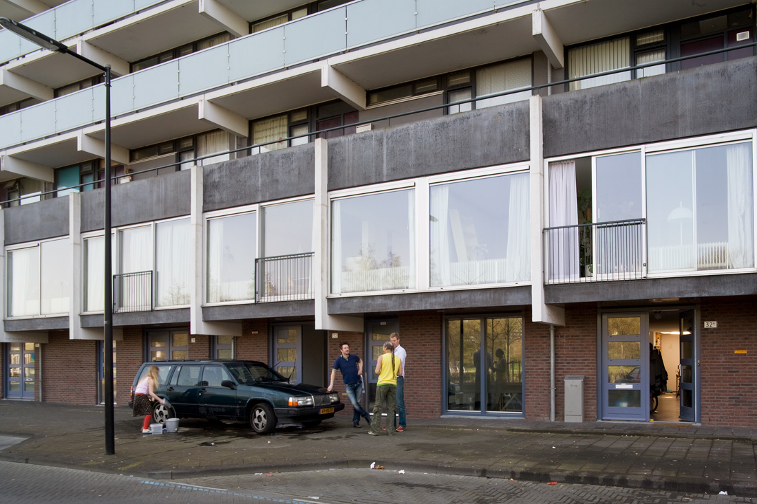 aangezicht van de plint van de gerenoveerde flats florijn in bijlmermeer met mensen op de stoep met een auto die gewassen wordt