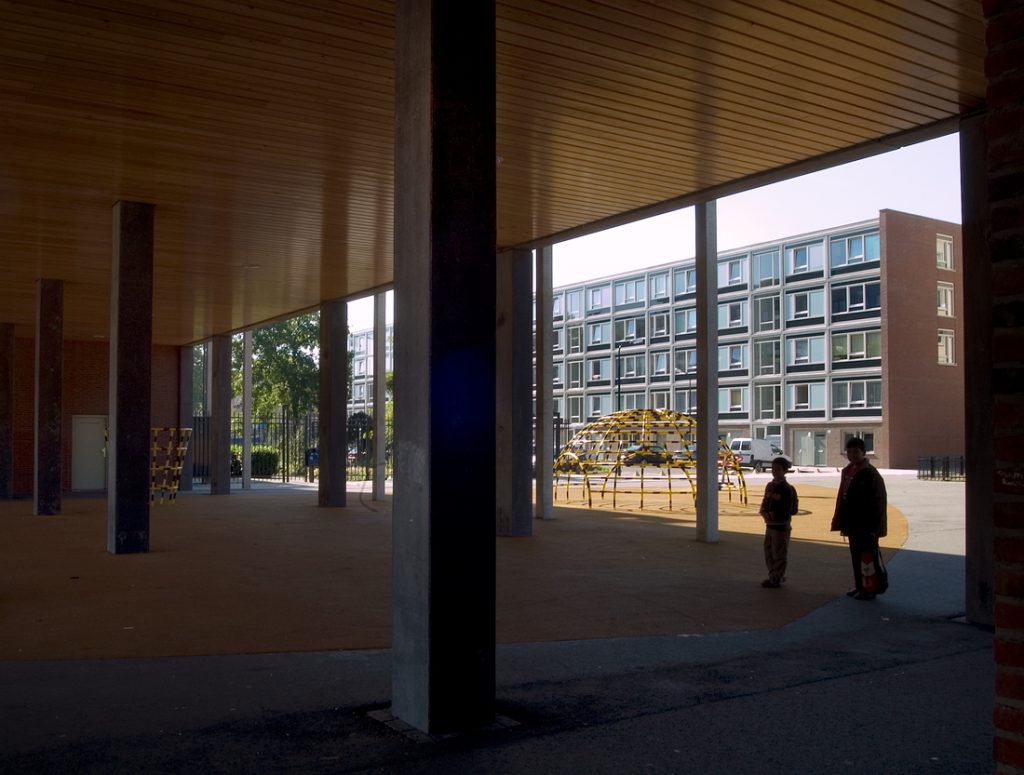 aanzicht van een ander flatgebouw in complex 50 en 117 vanuit de poort met een speeltuin ertussen en twee mensen