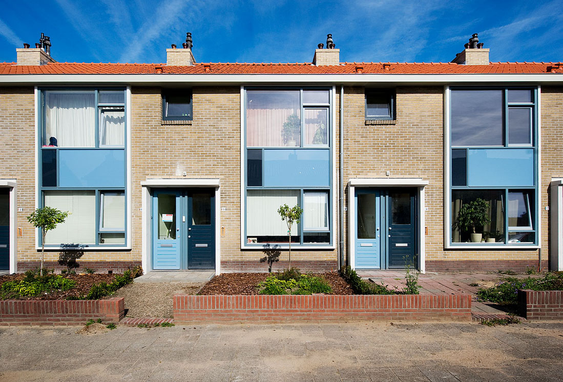 vooraanzicht van huizen aan de jan van galenstraat na renovatie met blauwe en oranje details en begroeiing in de voortuinen