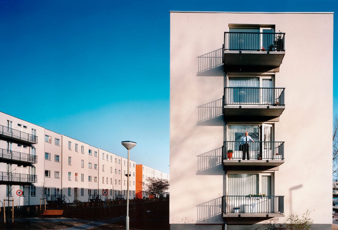 Foto van de kopgevel van een van de gerenoveerde woongebouwen van welschen in rotterdam met een man op het balkon