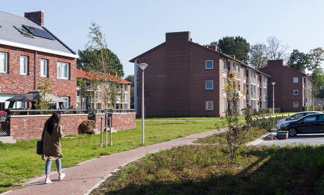 Foto van de gerenoveerde wijk de ganskuil in amersfoort met veel groen tussen de gebouwen en een buurtbewoonster lopend over een voetpad